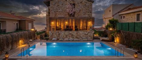 A stone building with a pool, lounge chairs, and lanterns.