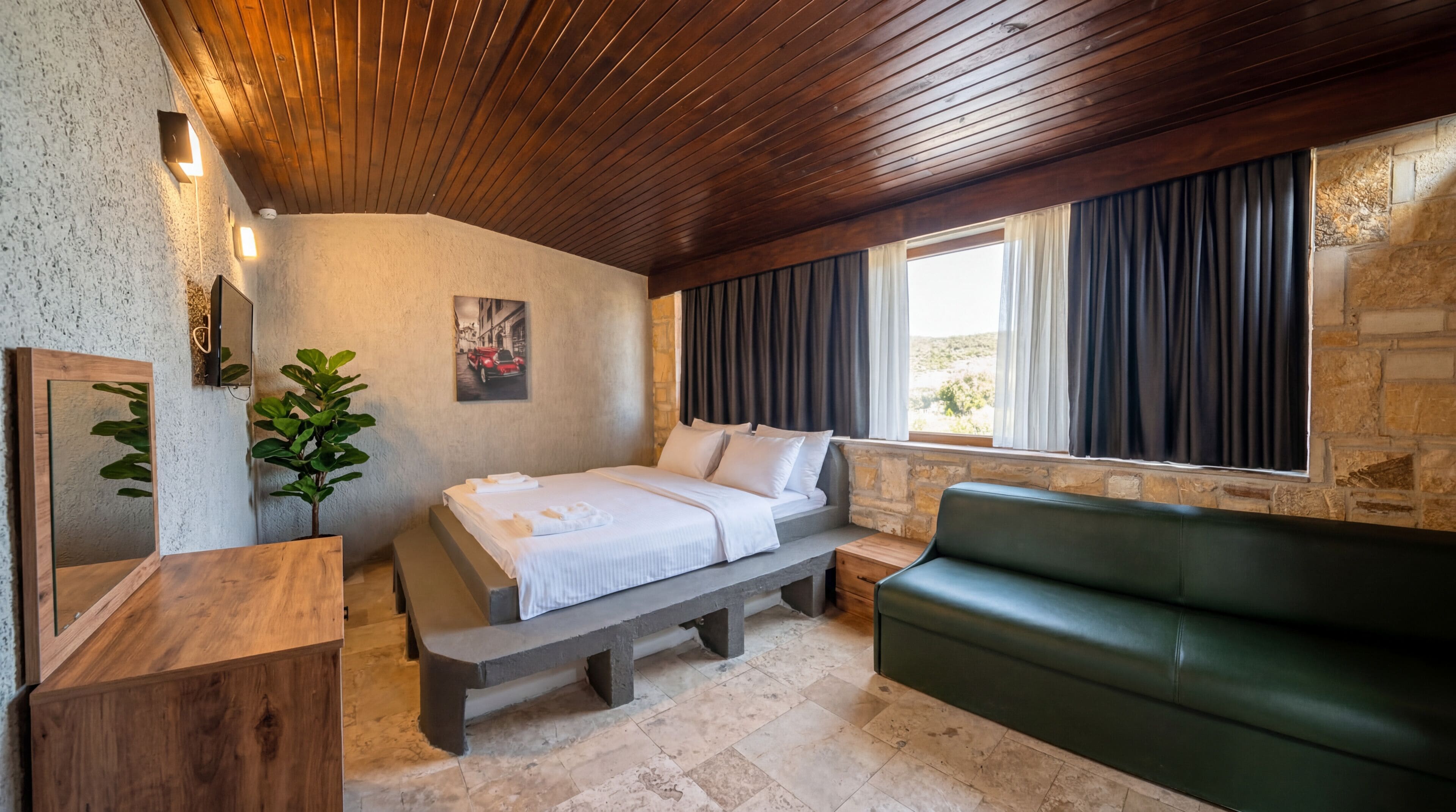 Un dormitorio con una cama, un sofá verde, una pared de piedra, un techo de madera y una ventana con cortinas.