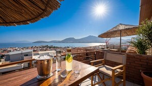 A wooden table with a bottle of drink, glasses, and a bucket of ice on a balcony overlooking a coastal city with mountains in the distance. - Stone House Foca Butik Otel (Foça)