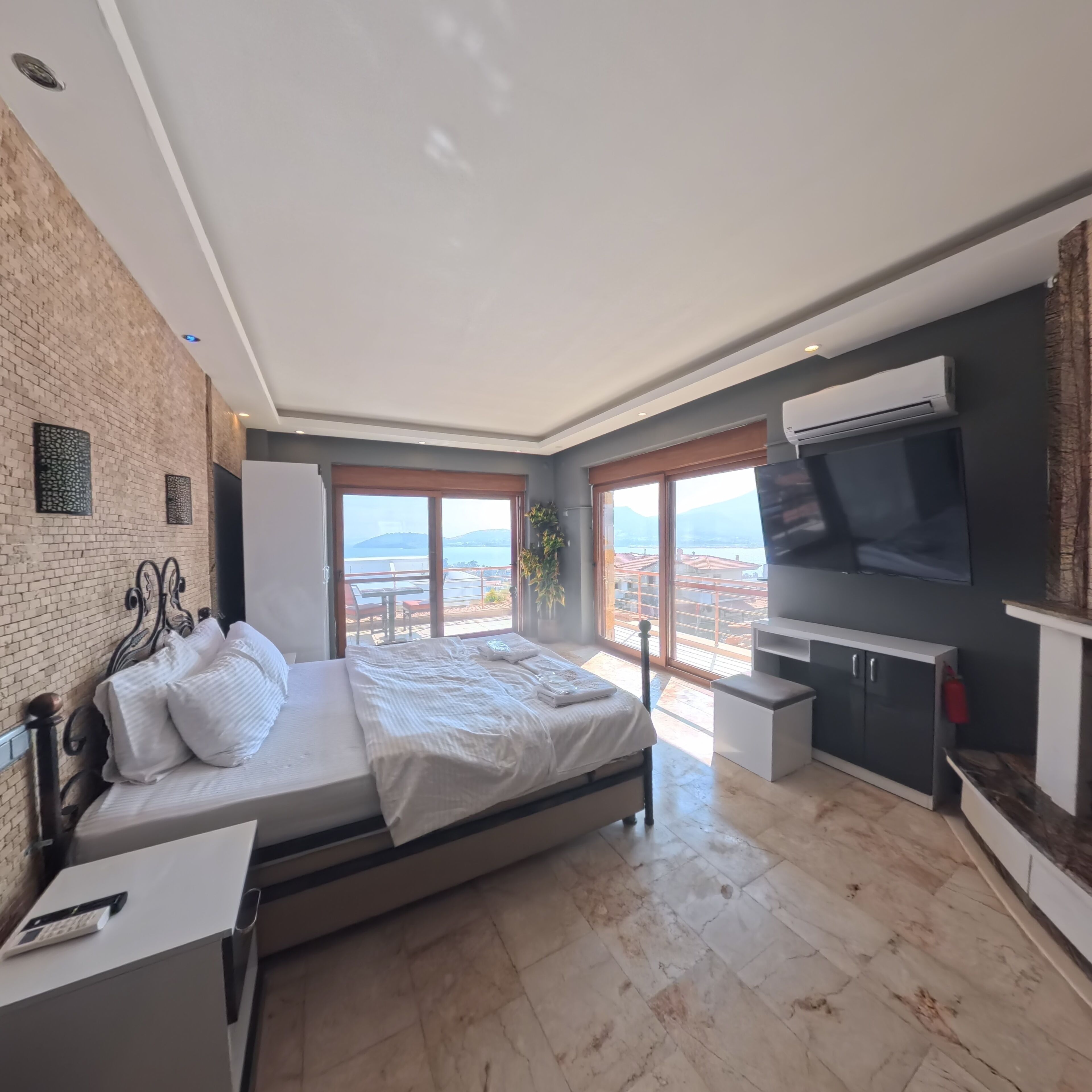A modern bedroom with a bed, a desk, a TV, and a balcony with a view.