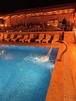 A swimming pool with lounge chairs and a thatched-roof structure.