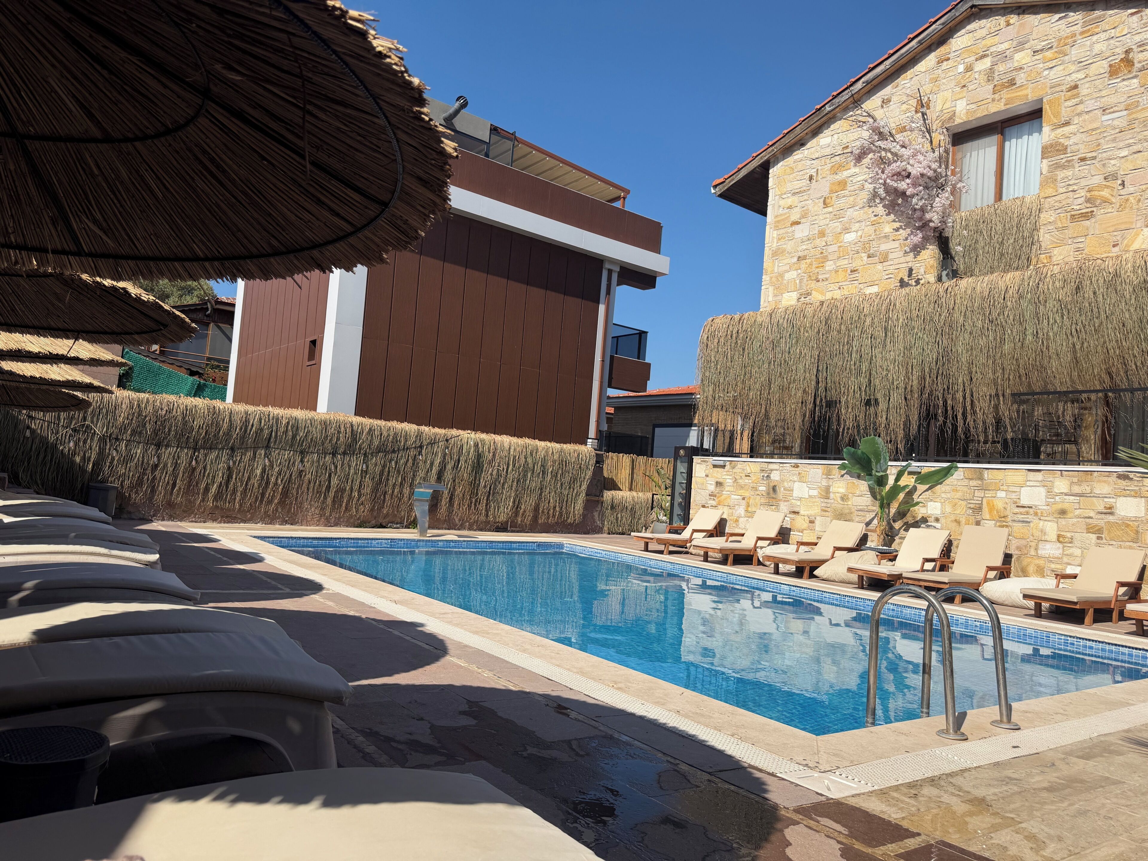Une piscine avec des chaises longues, un parasol en chaume et des bâtiments en pierre.