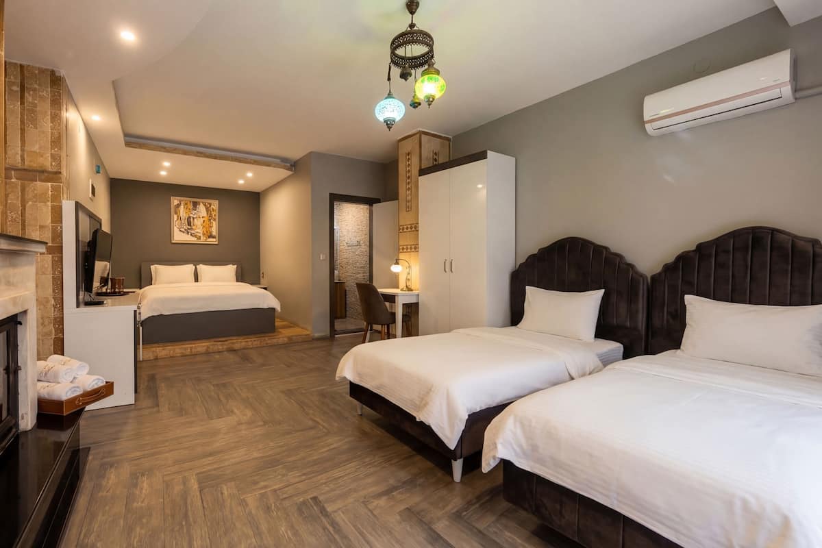 A hotel room with a fireplace, two beds, a desk, and a shower area.