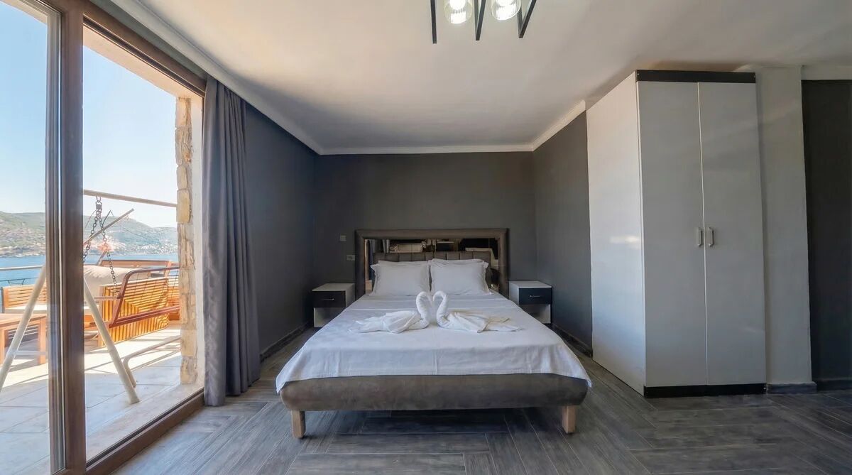 A hotel room with a bed, a wardrobe, a nightstand, and a large window with a view of the sea.