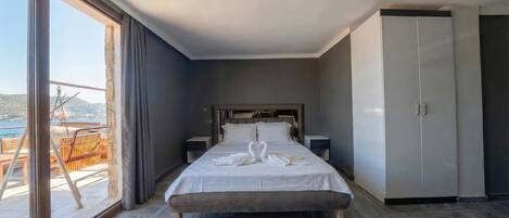 A hotel room with a bed, a wardrobe, a nightstand, and a large window with a view of the sea.