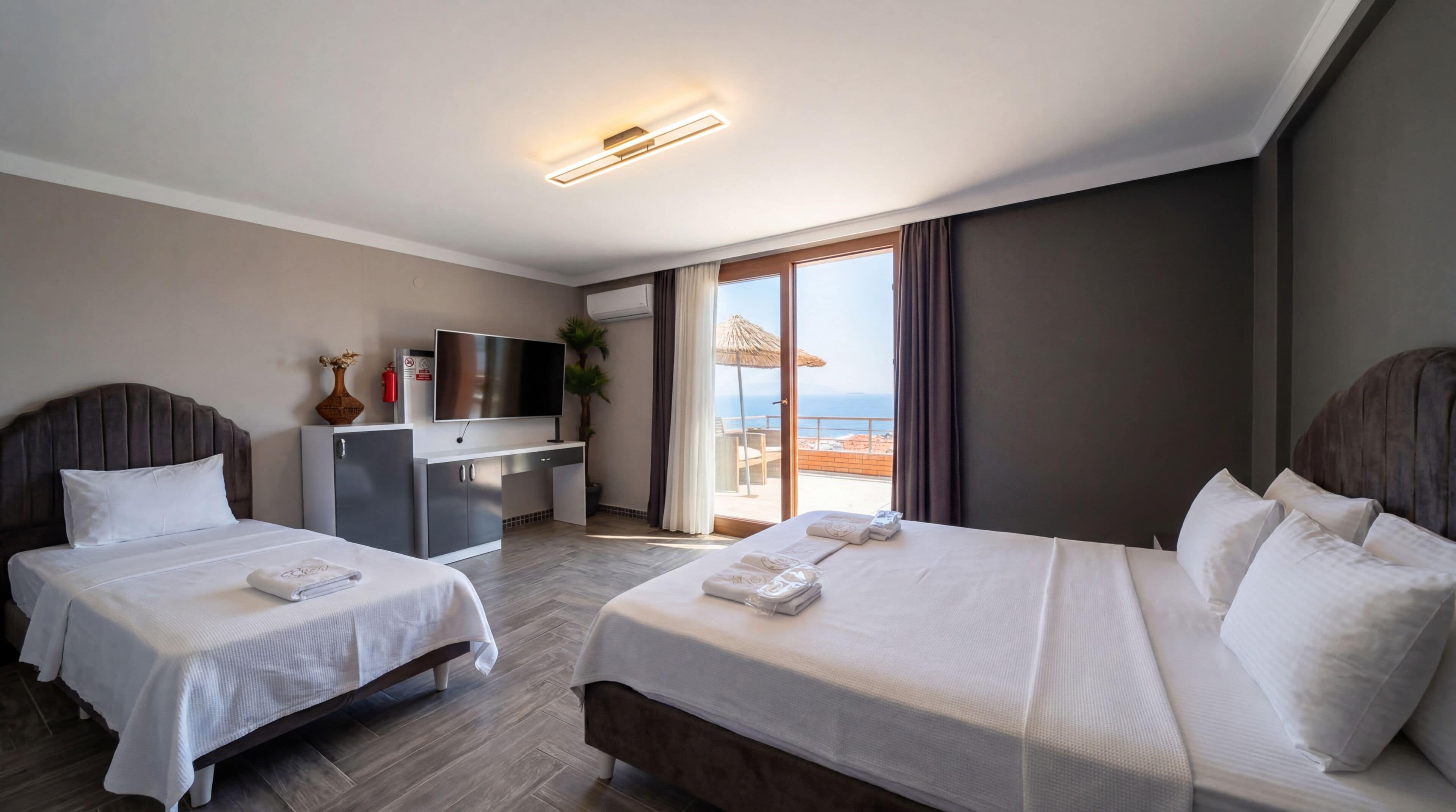 A hotel room with two beds, a desk, a TV, and a balcony with a view.