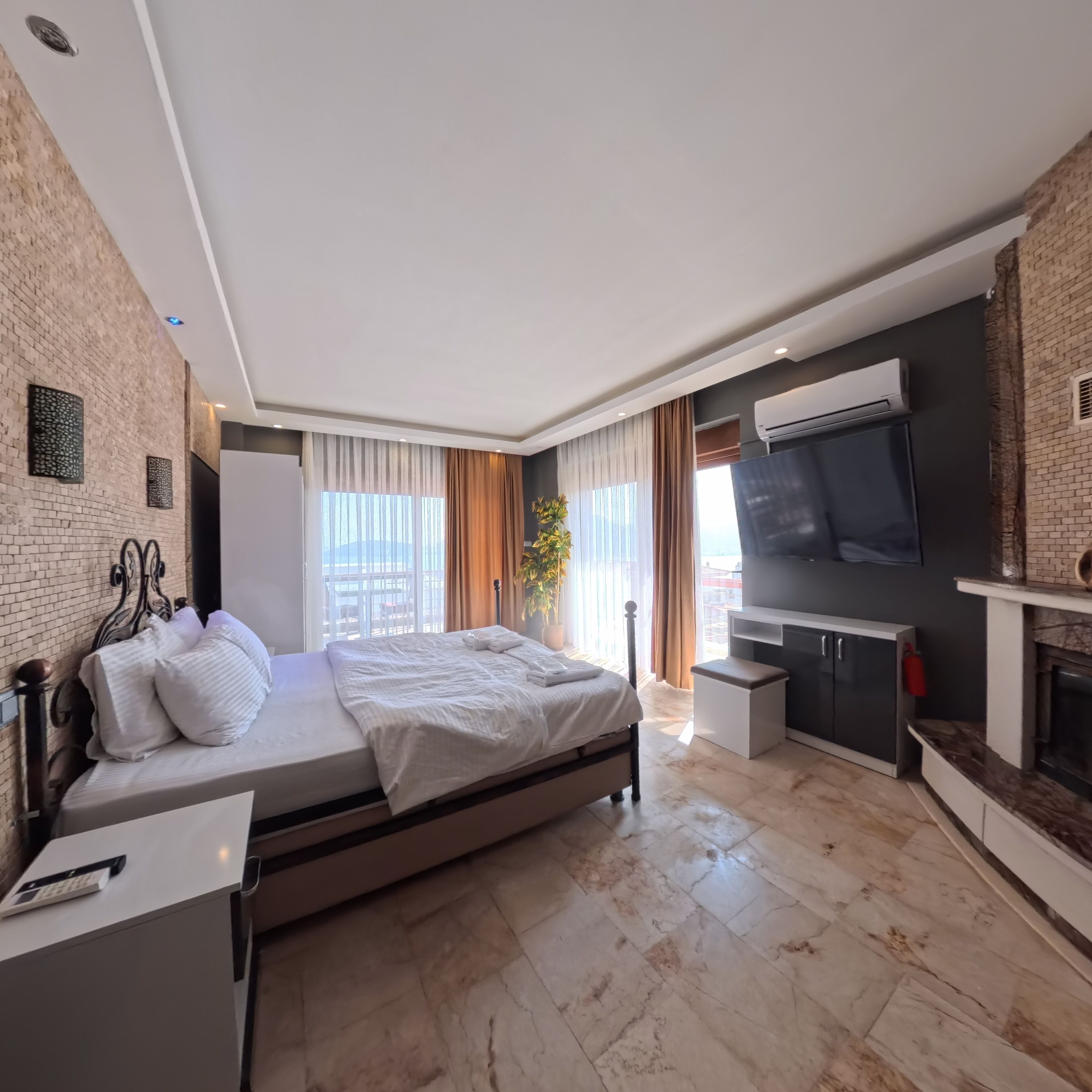 A modern bedroom with a large bed, a TV, a fireplace, and a balcony with a view.
