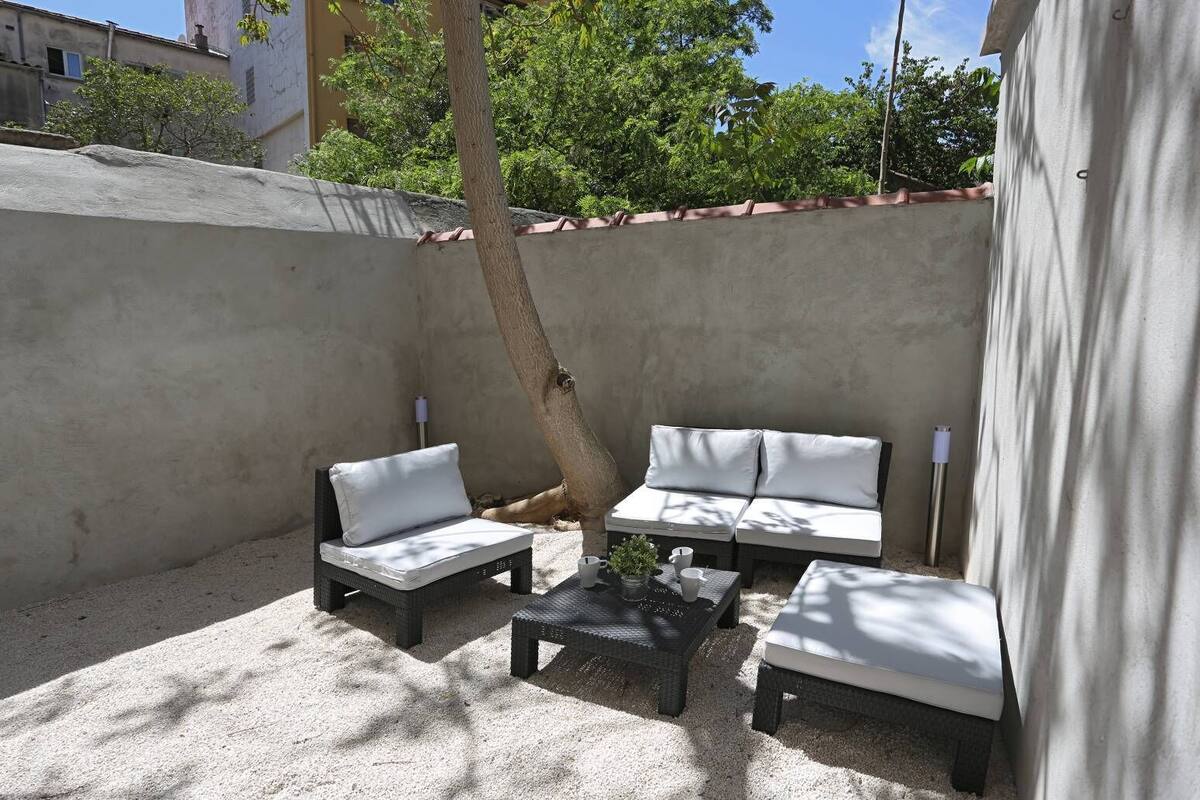 Un espace patio comprenant deux canapés blancs avec coussins, une petite table et un arbre qui offre de l’ombre.