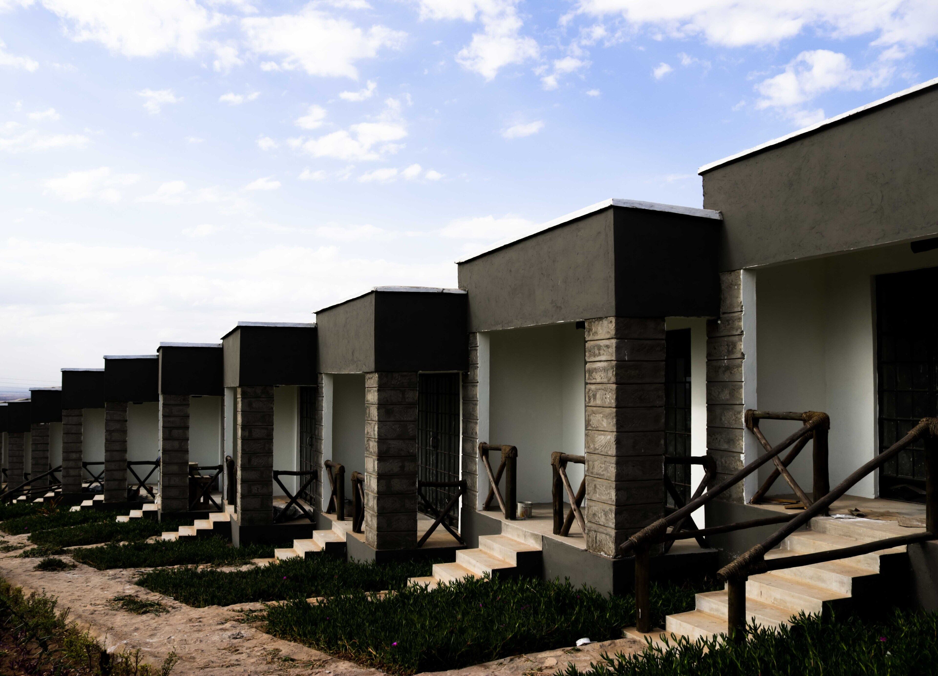 A row of modern, minimalist hotel rooms with concrete pillars and wooden railings.