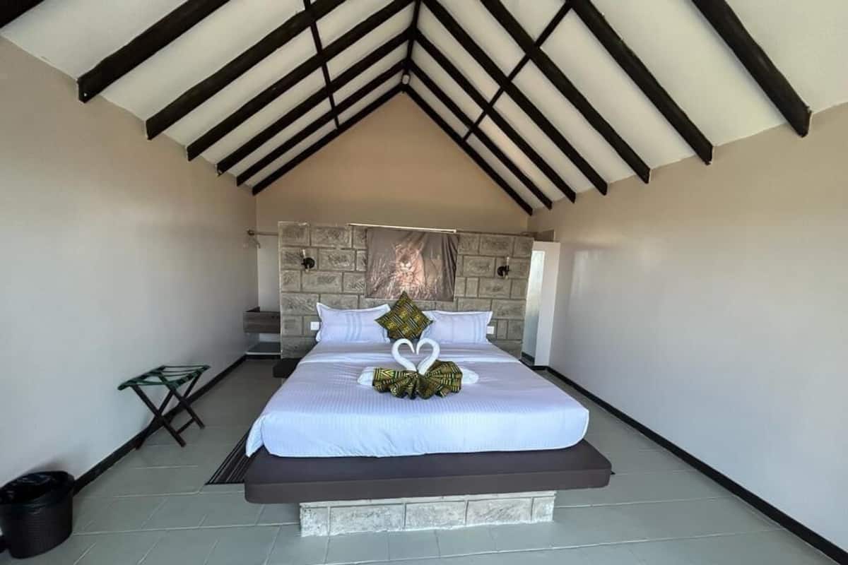 A bedroom with a high ceiling, a stone headboard, a bed with white bedding, and a heart-shaped decoration on the bed.