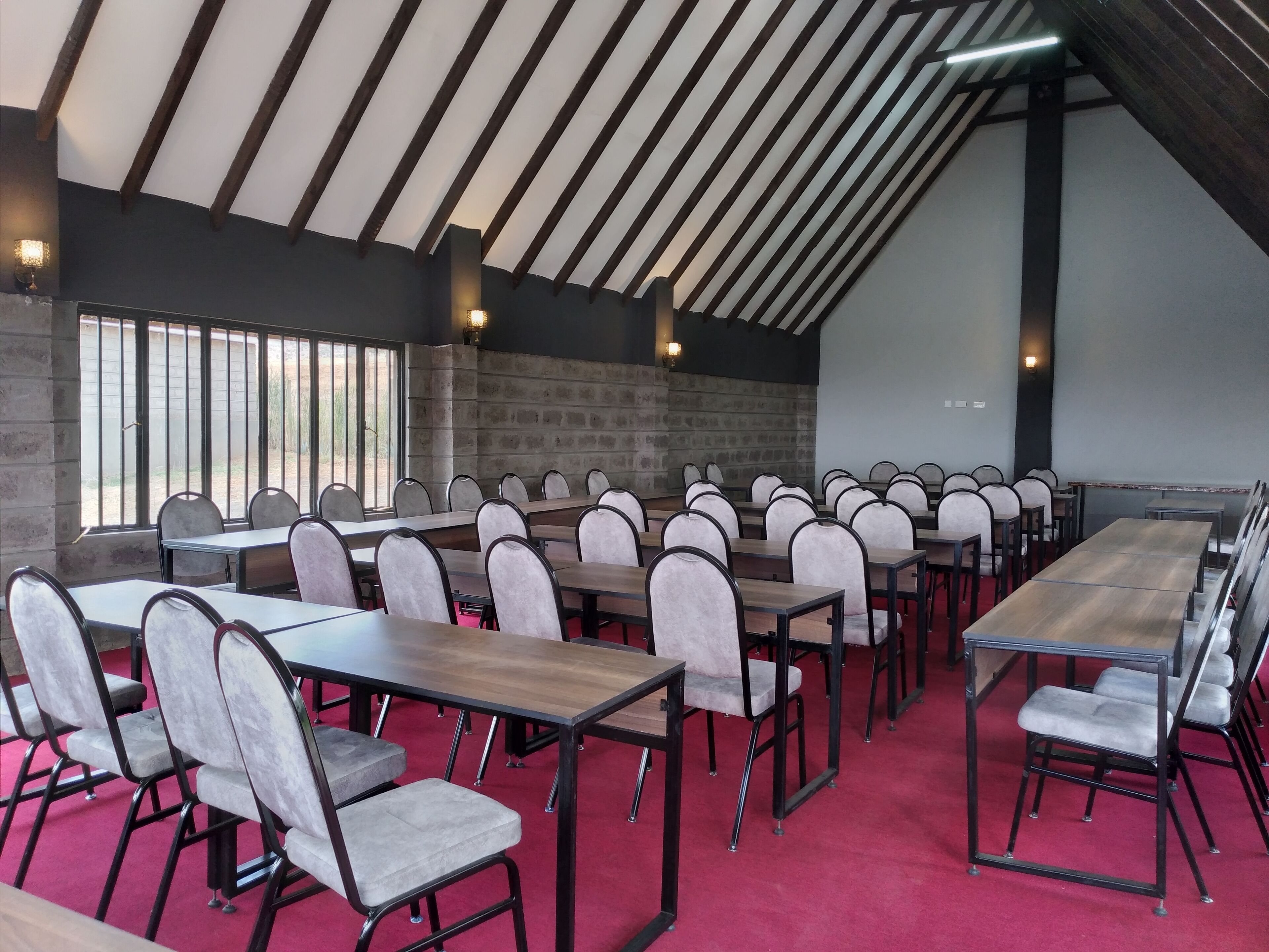 A conference room with multiple tables and chairs, a sloped ceiling with wooden beams, and a stone wall.