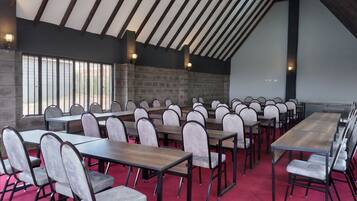 A conference room with multiple tables and chairs, a sloped ceiling with wooden beams, and a stone wall.