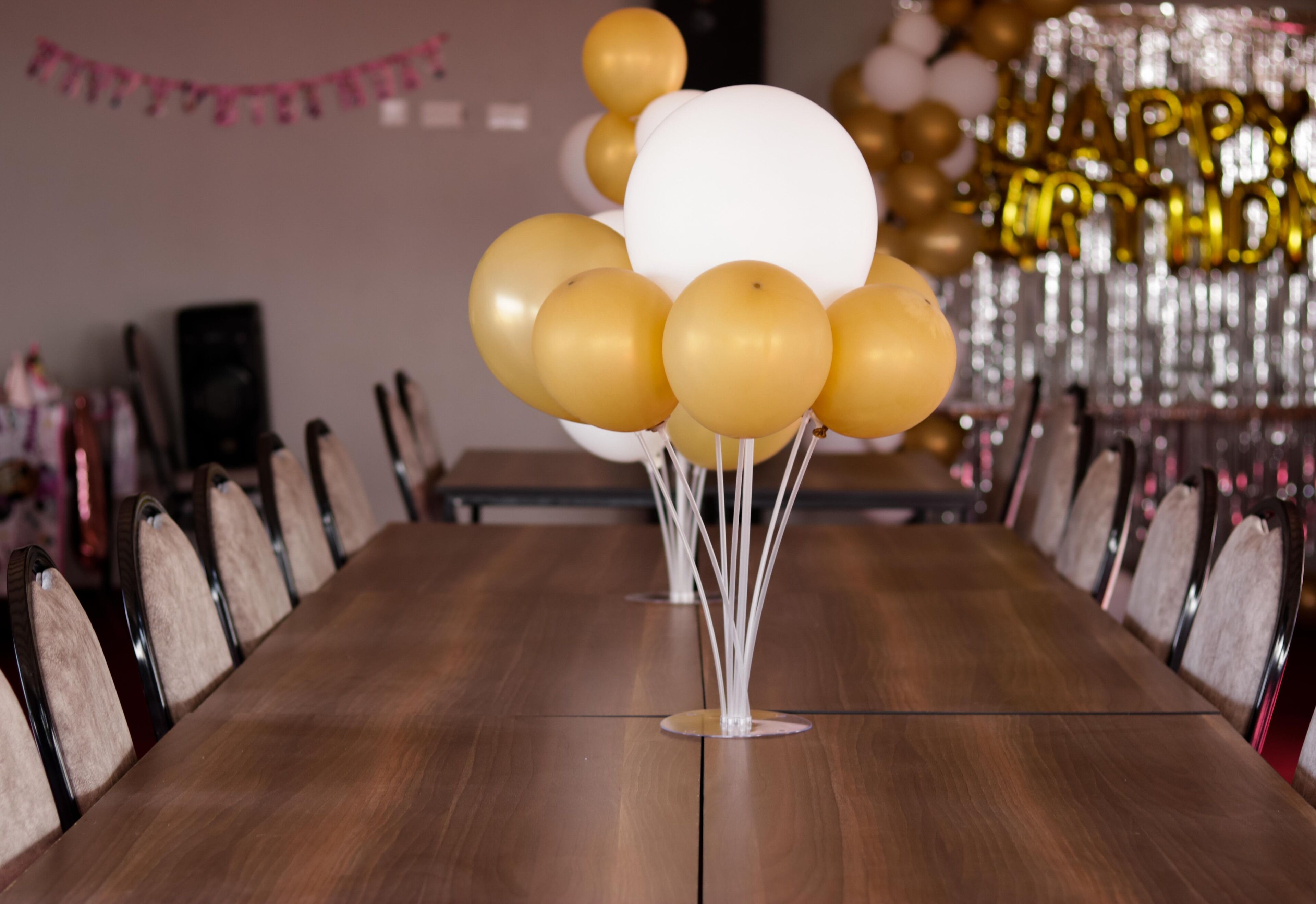 A long wooden table with chairs, balloons, and a 'Happy Birthday' decoration in the background.