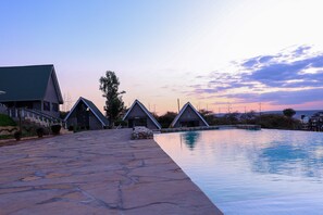 Un espace piscine agrémenté d’un chemin en pierre menant à un bâtiment doté d’un toit végétalisé et d’un design moderne.