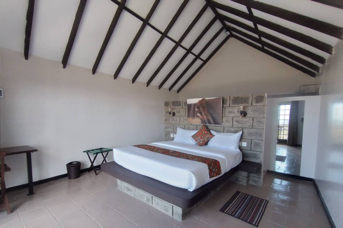 A bedroom with a bed, a small table, a trash bin, and a door leading to another room.