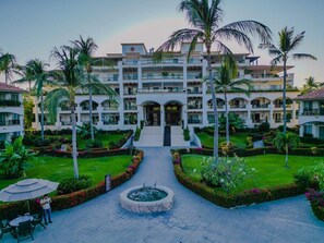 A multi-story hotel with a central courtyard, palm trees, and a fountain.