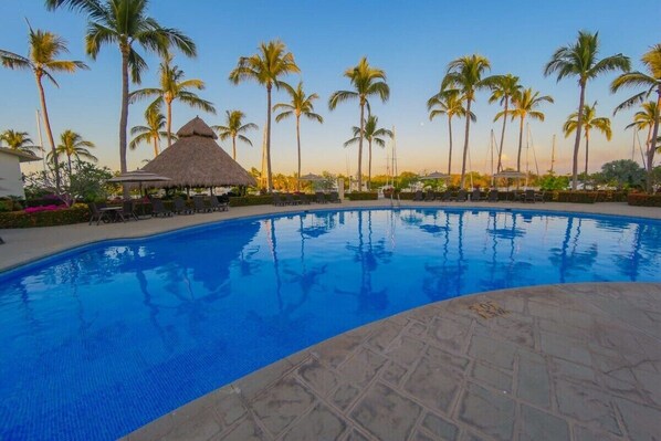 A swimming pool with lounge chairs and palm trees.