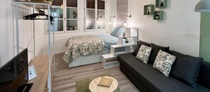 Une chambre à coucher de taille réduite, comprenant un lit, un canapé, une petite table et une fenêtre avec des rideaux.