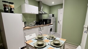 A compact kitchen with a dining area, white appliances, and a green wall. - 🌿 L'Oliveraie 🌿 (Brioude)