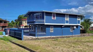 Une maison à deux étages, avec une façade bleue et un balcon à l’étage supérieur.