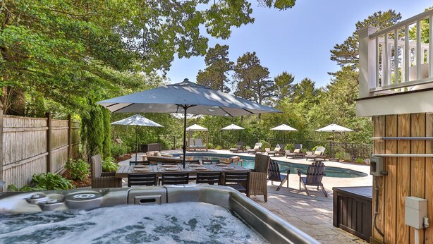 En trädgård med en bubbelpool, en pool, utemöbler och parasoller.