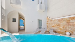 Un área de piscina con vista despejada al mar, un edificio blanco con muro de piedra y sillones de descanso.