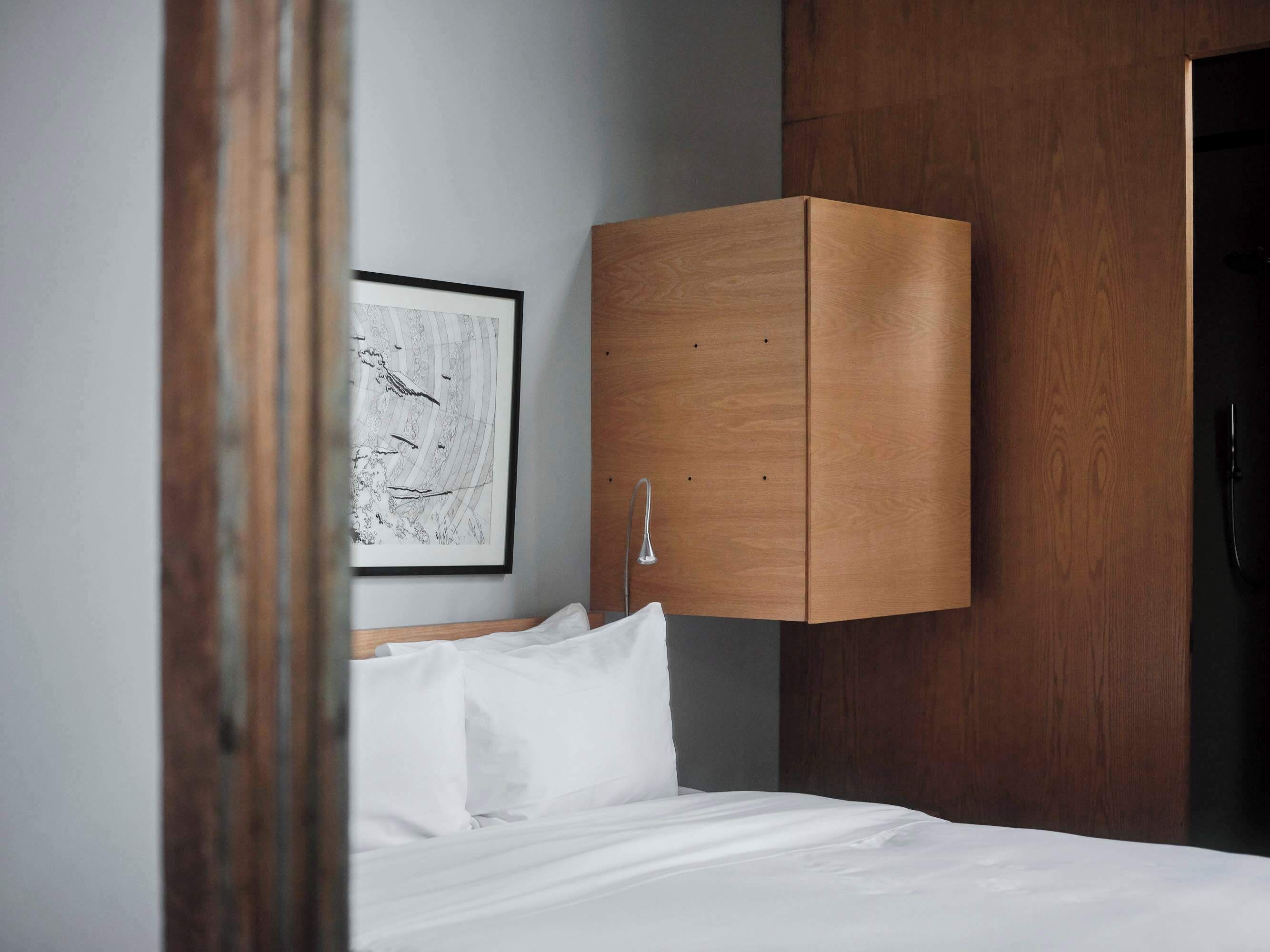 A bedroom with a wooden wardrobe, a bed with white bedding, and a framed abstract artwork on the wall.