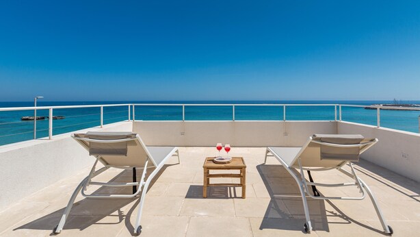 A balcony with two lounge chairs, a small table, and two glasses of red wine. - 2940 Palma Residence- Appartamento Notos by Barbarhouse (Melendugno)
