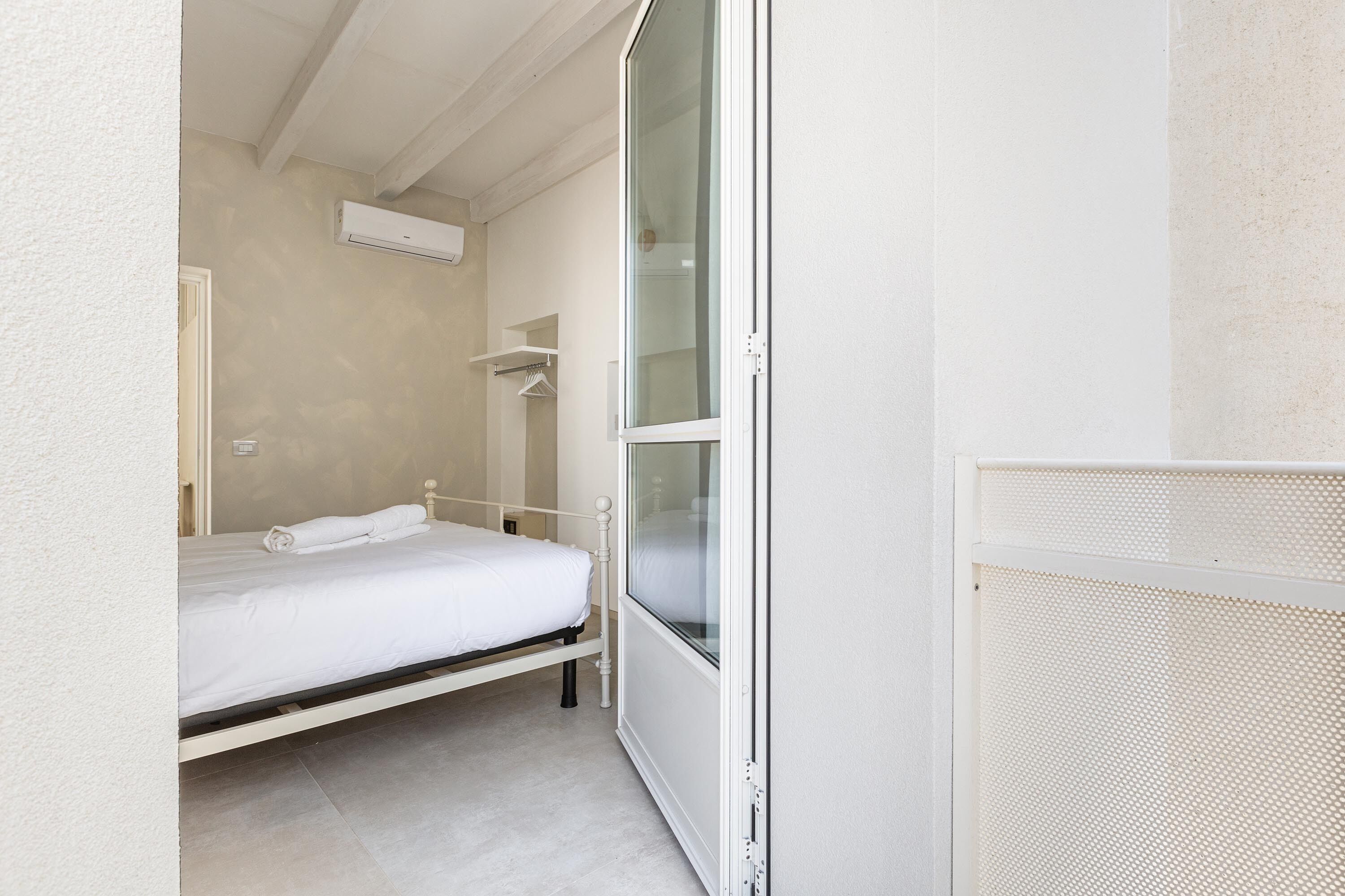 Una habitación pequeña y limpia con una cama individual, una ventana y aire acondicionado instalado en la pared.