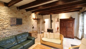 Una sala rústica con paredes de piedra, un sofá de cuero verde, un sofá de mimbre y un aparador de madera.