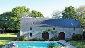 Un edificio de piedra con piscina, un patio cubierto y un césped.