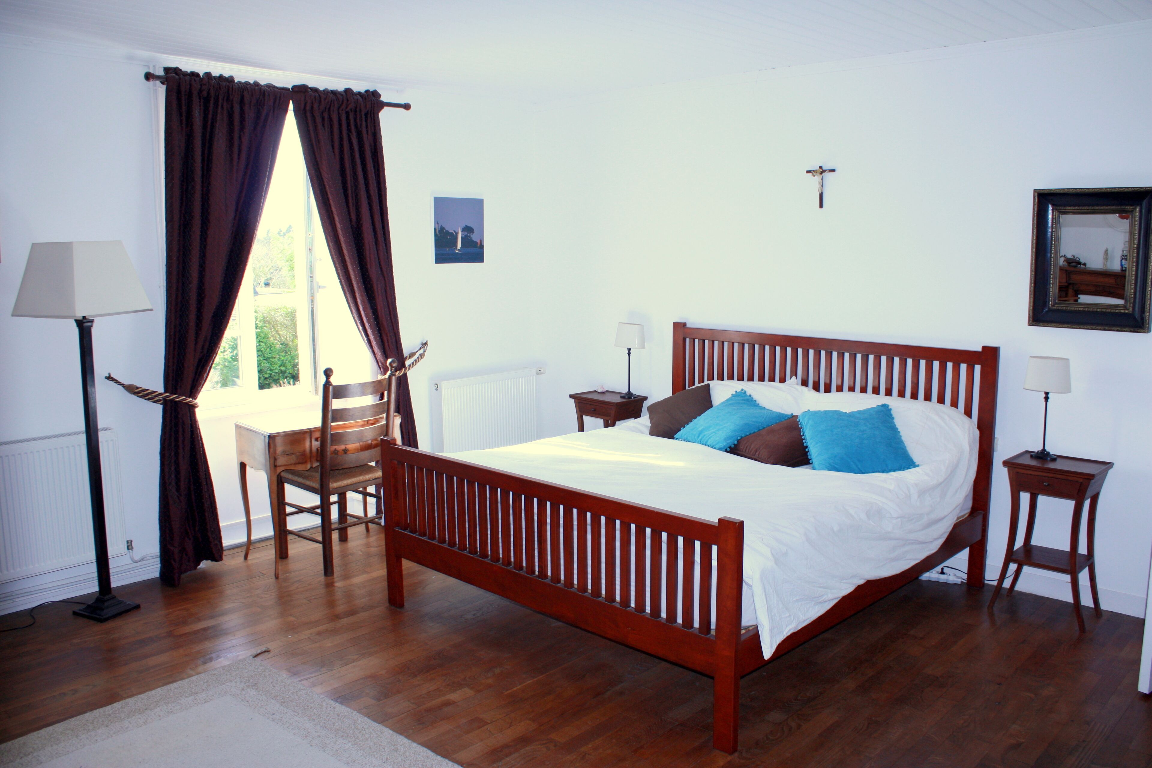 A bedroom with a wooden bed, two bedside tables, a chair, a radiator, and a window with curtains.