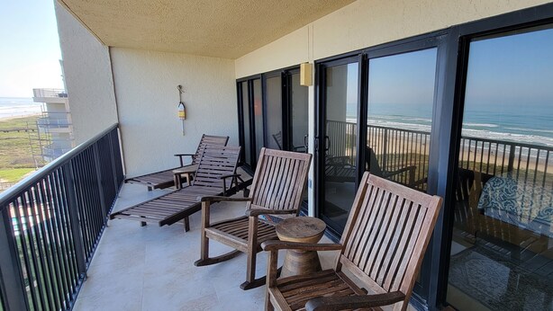 Een balkon met houten meubels en uitzicht op het strand.