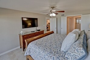 A bedroom with a bed, a TV, a ceiling fan, and a door leading to a bathroom. - Spi Fun And Sun 2 Bedroom Condo by RedAwning (South Padre Island)