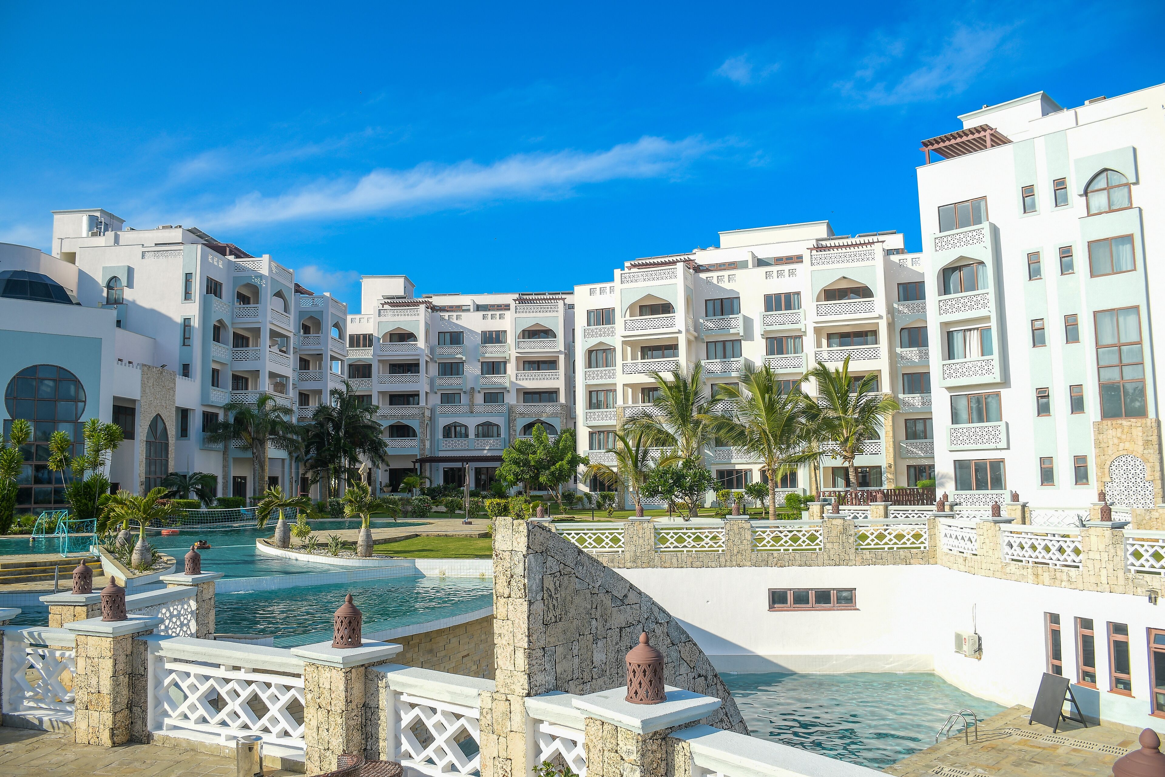 A resort with multiple-story buildings, a swimming pool, and palm trees.