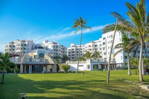Un hotel con varios edificios blancos, un césped cuidado y palmeras.