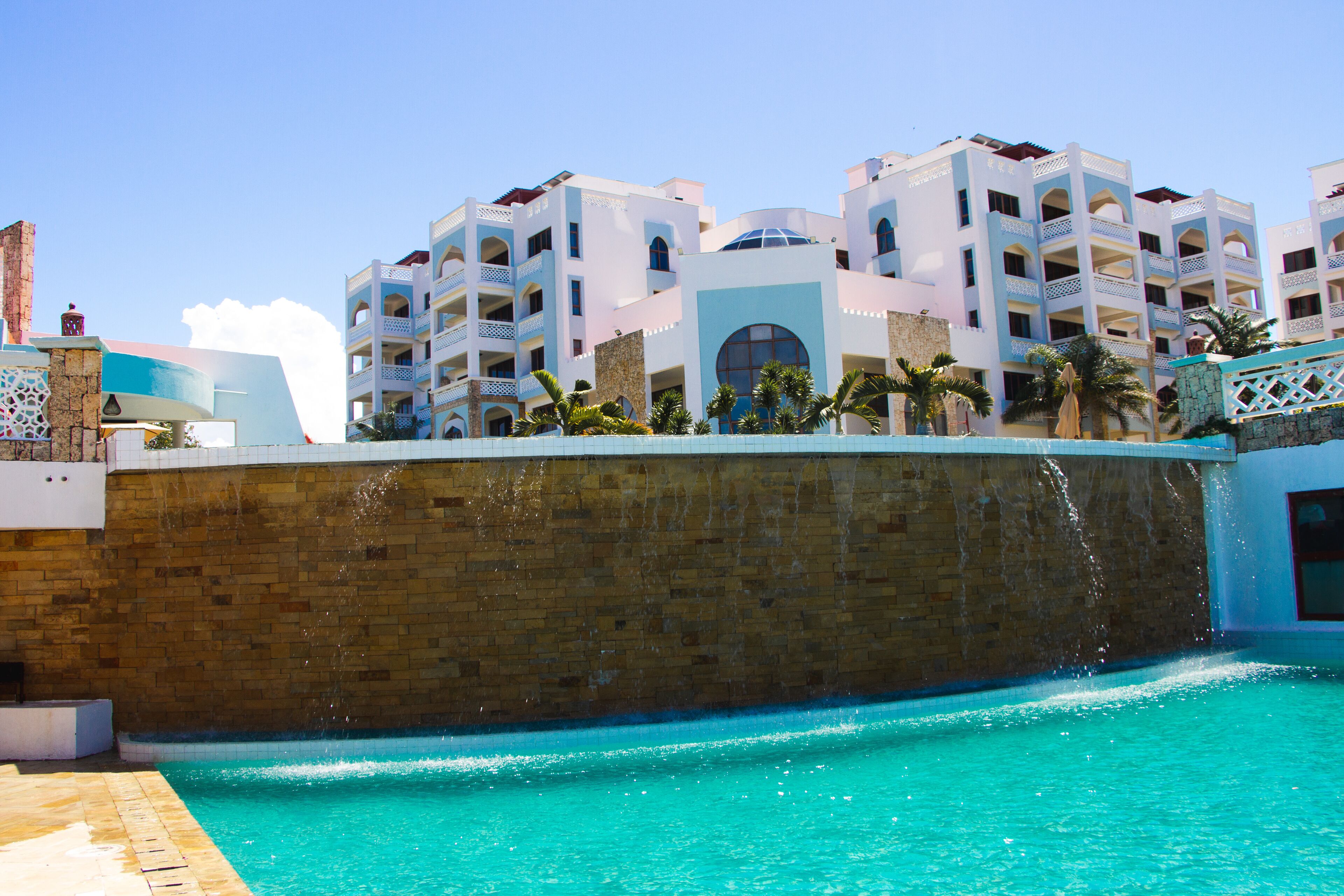 Um hotel com piscina, várias varandas e uma parede de pedra.