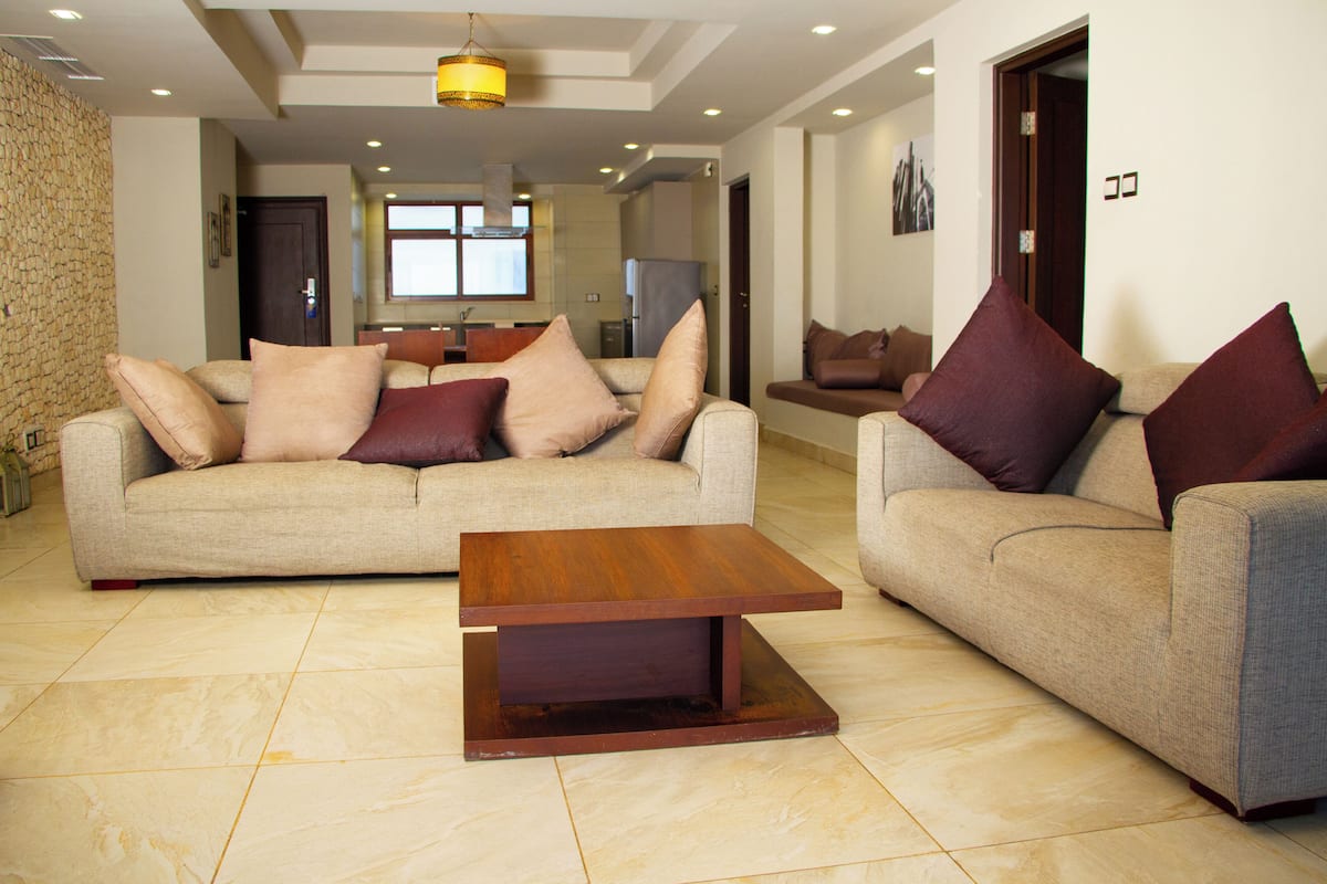 A spacious living room with two sofas, a wooden coffee table, and a kitchen in the background.