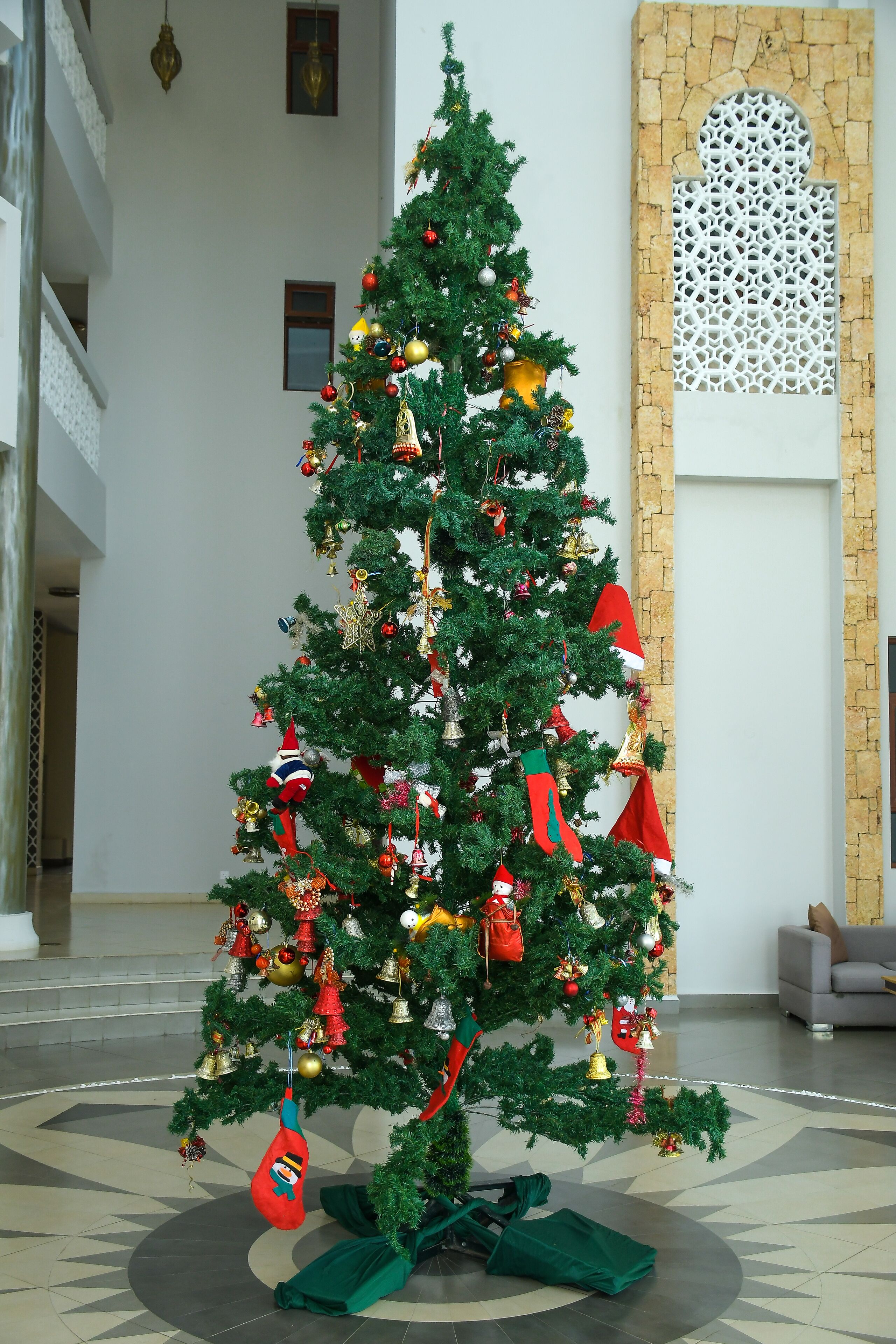 A Christmas tree in a lobby with a stone wall and a sofa in the background.