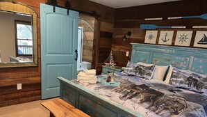 A bedroom with a wooden bench, a bed with a nautical-themed headboard, and a wall with nautical decorations. - COZY RIVER FRONT CABIN (Blue Ridge)