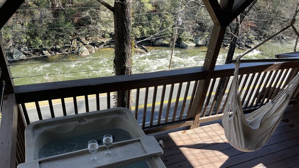 A wooden deck with a hot tub and hammock overlooking a river. - COZY RIVER FRONT CABIN (Blue Ridge)
