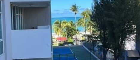 Une vue de rue avec un bâtiment sur la gauche, un ciel bleu dégagé et une personne qui marche sur le trottoir.