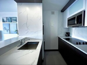 A modern kitchen with a marble countertop, a built-in sink, and a microwave.
