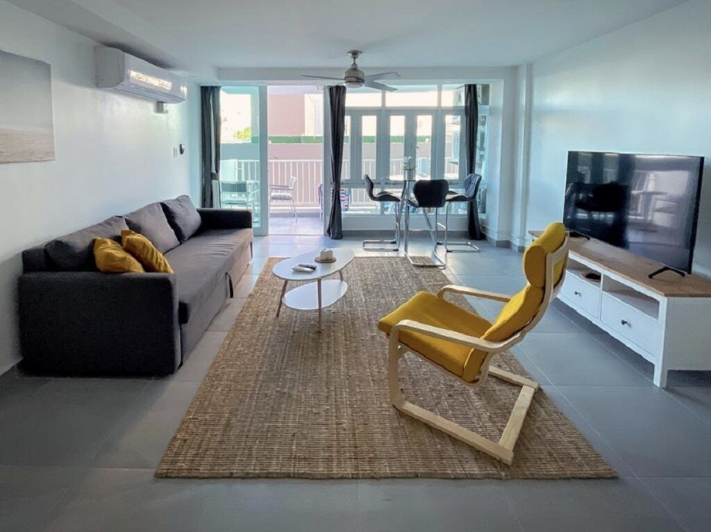 A modern living room with a sofa, a yellow armchair, a TV, and a balcony with chairs.