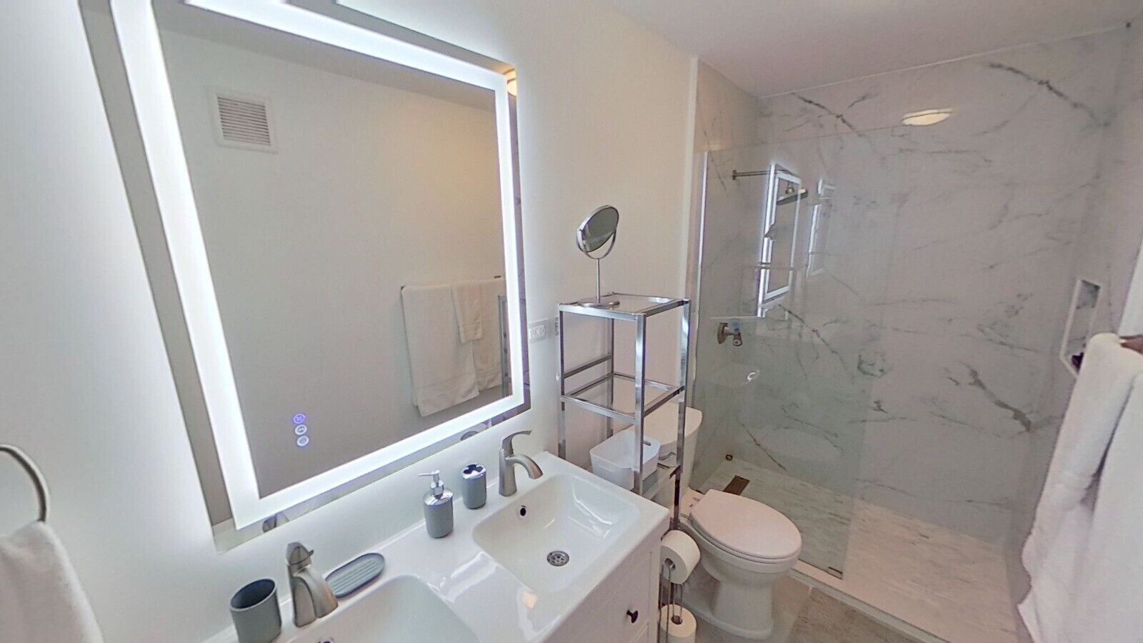 Un baño moderno con un espejo grande, un lavabo blanco, un inodoro y una ducha con mampara de cristal.