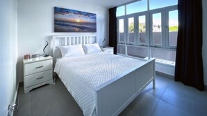 Ein Schlafzimmer mit Bett, Nachttisch, Deckenventilator, Fenster mit Vorhängen und einem Bild an der Wand.