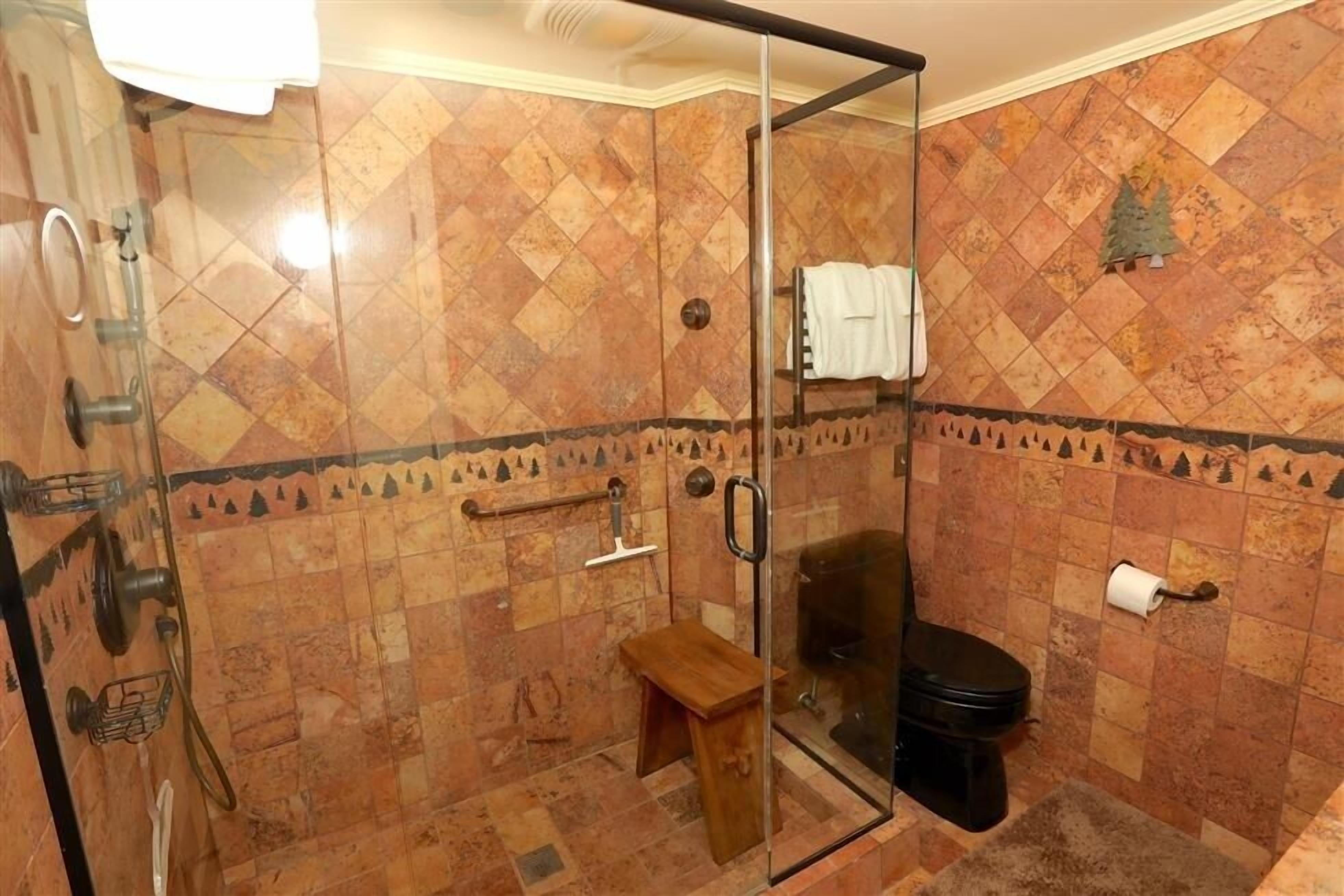 A bathroom with a glass shower enclosure, a wooden bench, a toilet, and a towel rack.
