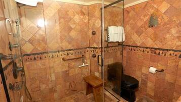 A bathroom with a glass shower enclosure, a wooden bench, a toilet, and a towel rack.