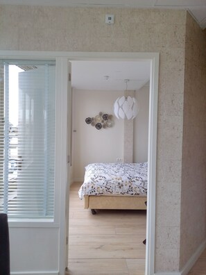 Quarto com cama, luminária no teto e termostato fixado na parede.