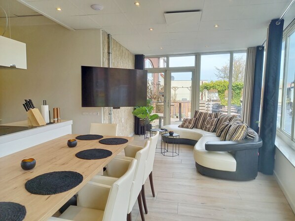 Una sala moderna con una mesa de comedor de madera, sillas blancas, un sofá con cojines a rayas y un ventanal con vistas al exterior.